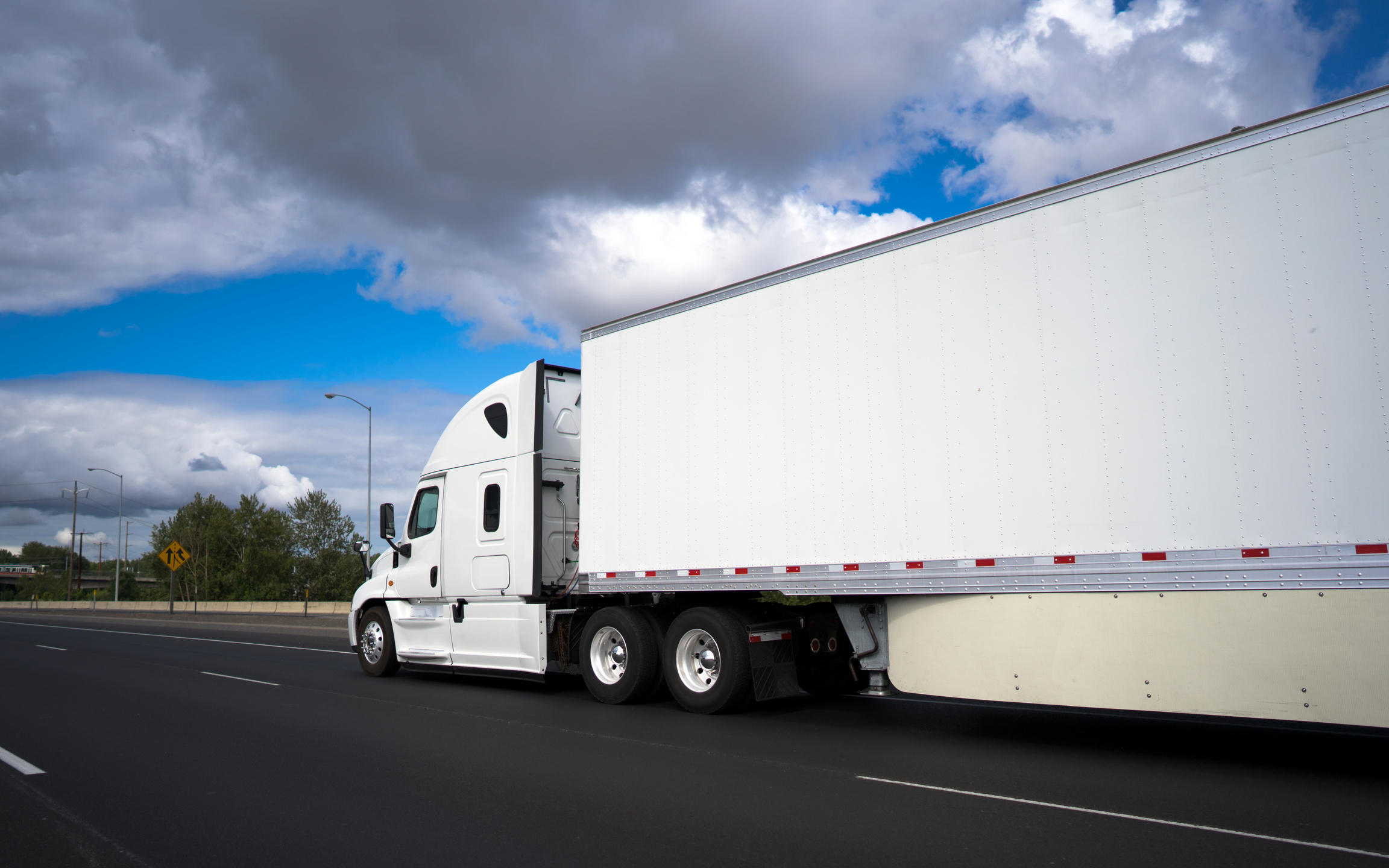 Long haul big rig semi truck transporting commercial cargo in dry van semi trailer on the wide highway with clouds sky